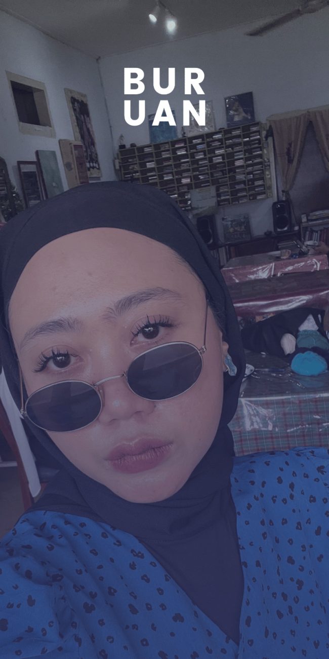 Aya Cannina, penyair perempuan asal Bekasi, menggunakan baju volkadot berwarna biru dan menggunakan kaca hitam dengan jilbab hitam.