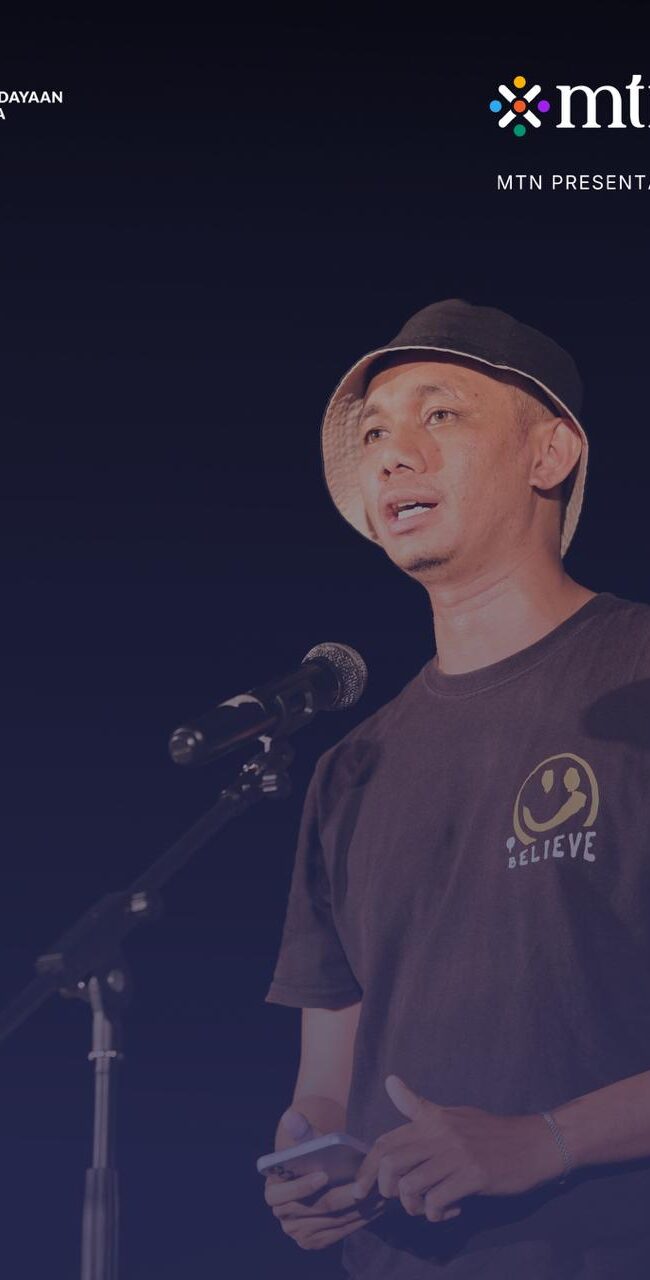 Cover Puisi Ricky Ulu di Buruan.Co. Ricky Ulu menggunakan kaos hitam dan topi bundar hitam saat membacakan puisi. Terdapat logo Kemenbud, MTN, dan Buruan.co.