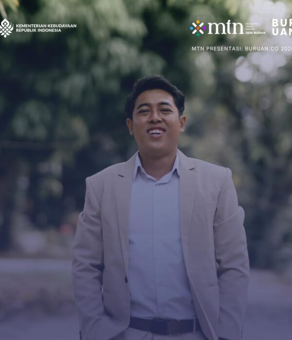 Alfa Zain mengenakan jas krem dan kemeja putih berpose dan tersenyum. Foto setengah badan.